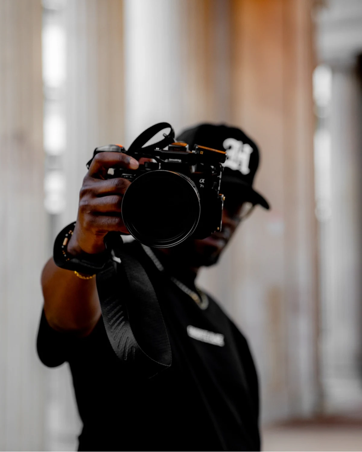 Ian Bennett at the Voorhies Memorial in Denver, all black, Sony Alpha and cine glass raised to the lens — Action beat