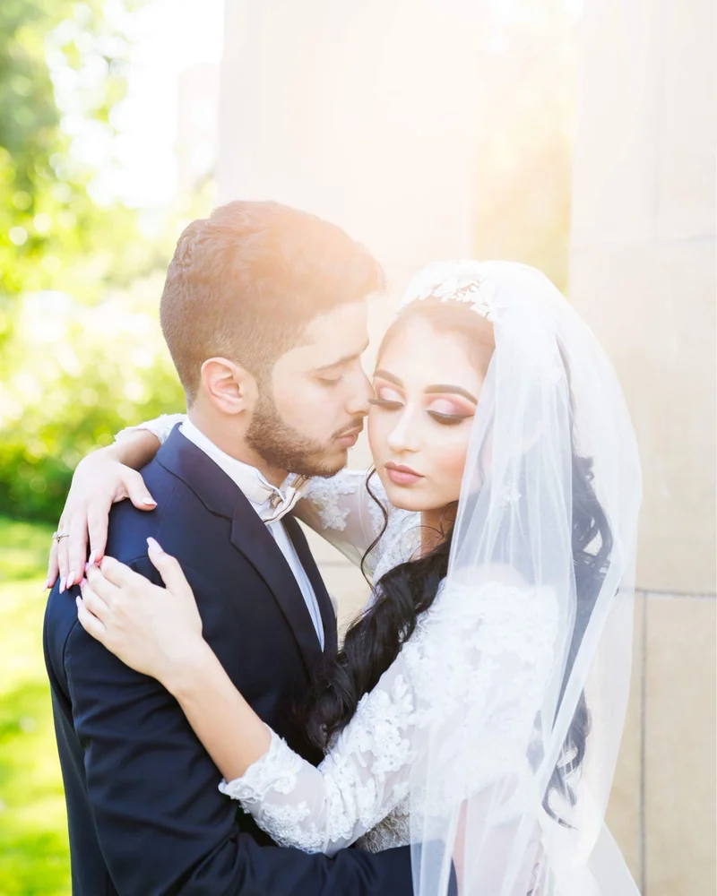 Bride and groom in a warm backlit embrace, her veil catching the sun